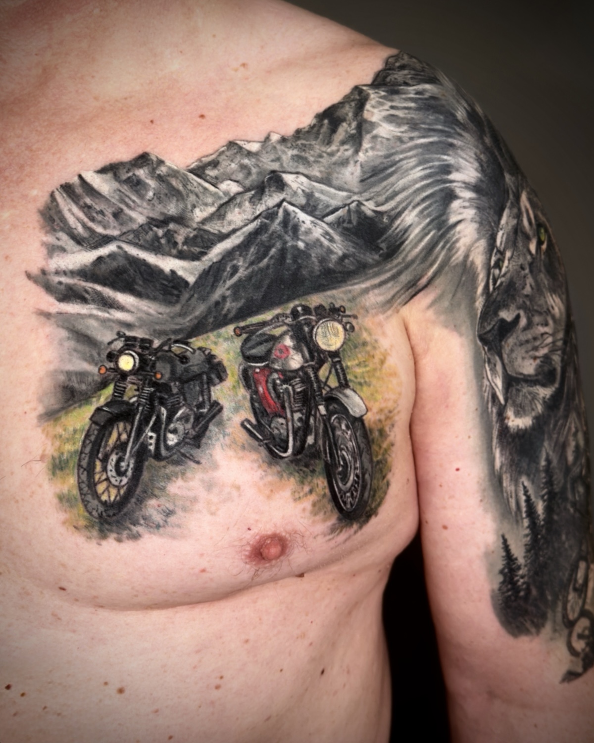 Farb Tattoo Deggendorf — Color Tattoo zwei Vintage Motorräder vor Berglandschaft auf der Brust von Luca Limito Tattoo, Atelier Voltaire Tattoo Studio / Color tattoo Deggendorf — two vintage motorcycles in front of mountain landscape on chest by Luca Limito at Atelier Voltaire Tattoo Studio
