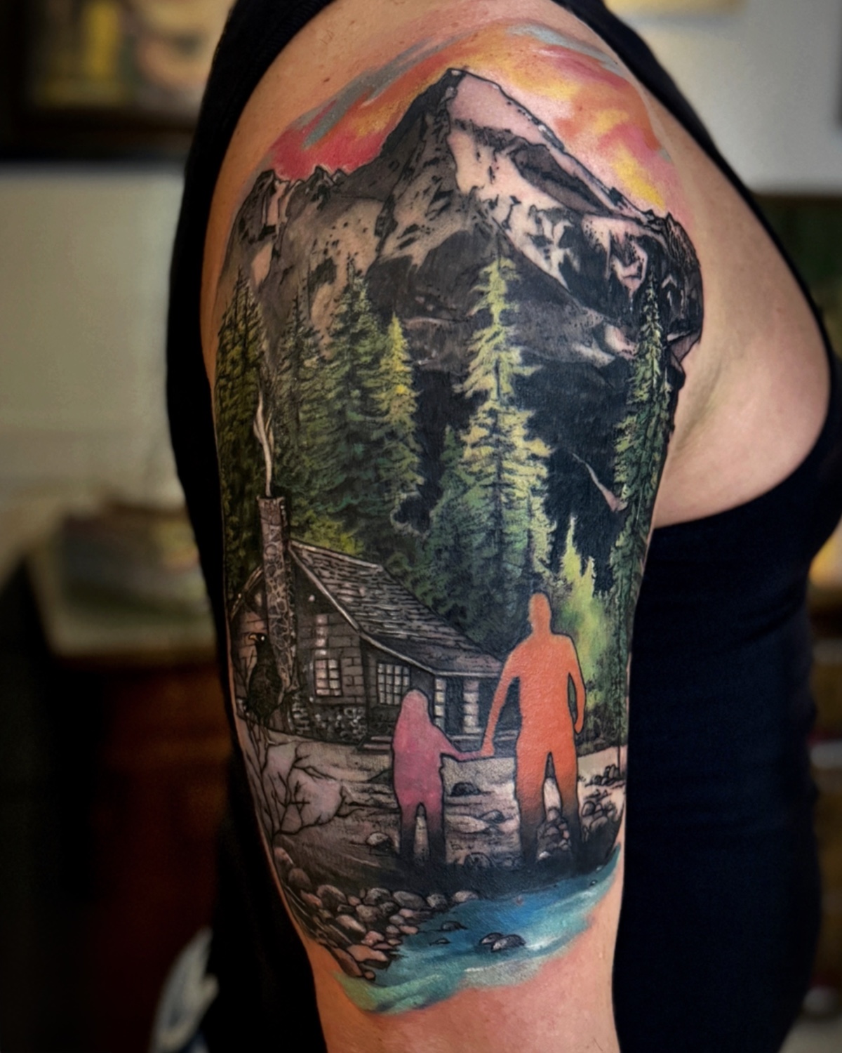 Color Tattoos Deggendorf — Farb Tattoo Berglandschaft mit Hütte, Wald und farbigen Silhouetten am Oberarm, Tätowierer Deggendorf Luca Limito, Atelier Voltaire Tattoo Studio / Color tattoos Deggendorf — mountain landscape with cabin, forest and colored silhouettes on upper arm by Luca Limito at Atelier Voltaire Tattoo Studio
