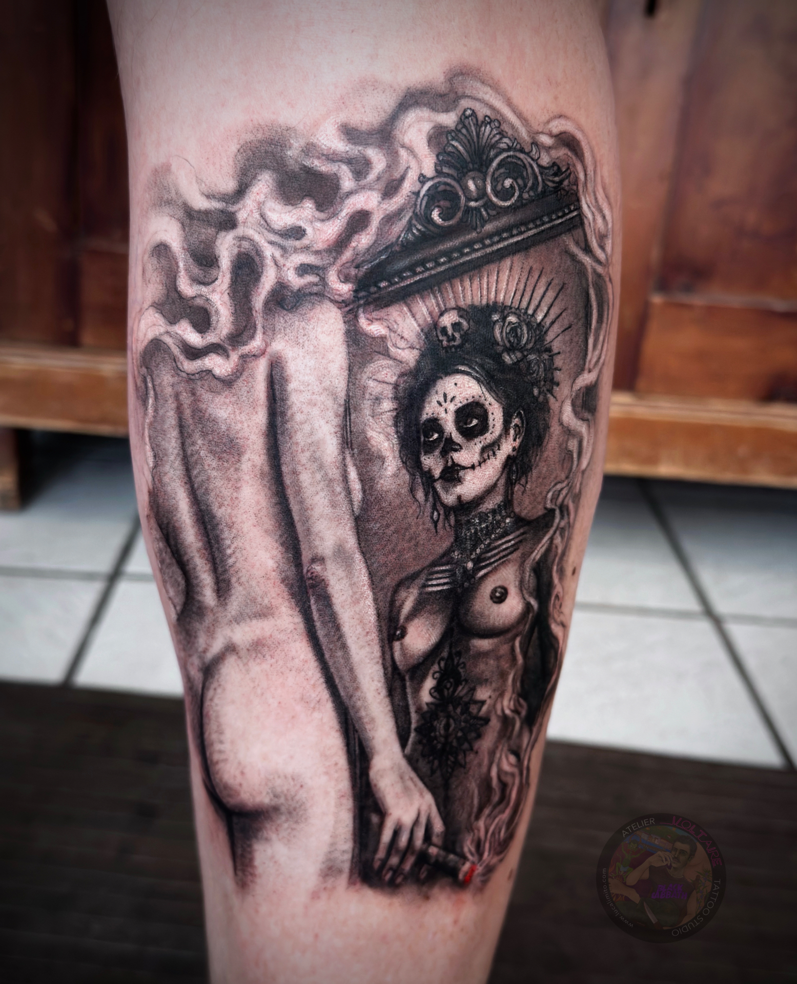 Catrina Spiegel Black & Grey Tattoo von Luca Limito – Atelier Voltaire Tattoo Studio Deggendorf — surreale nackte Frau mit Rauchkopf und Zigarre vor ornamentalem Spiegel, dessen Spiegelbild eine La Calavera Catrina Zuckerschädel-Reflexion zeigt, am Bein / Catrina mirror black and grey tattoo by Luca Limito at Atelier Voltaire Tattoo Studio Deggendorf — surreal nude woman with smoke head and cigar before an ornate mirror reflecting a La Calavera Catrina sugar skull on leg