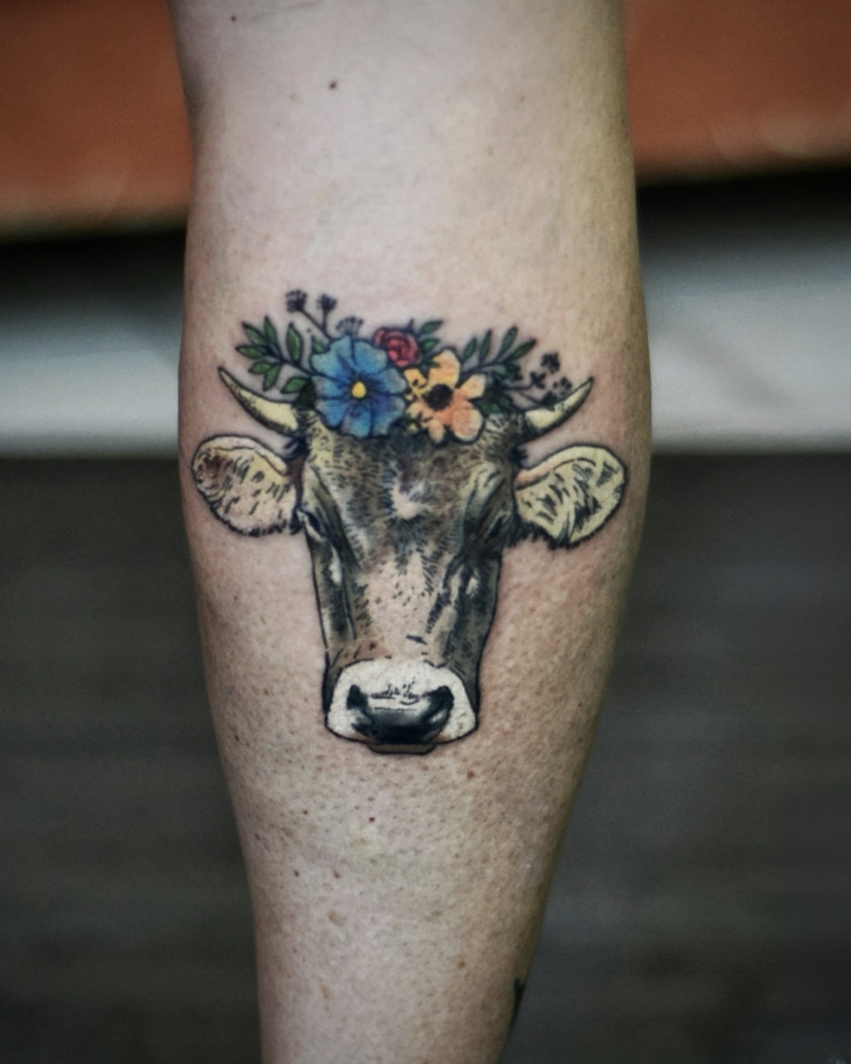 Animal Tattoo Deggendorf — Color Kuh mit Blumenkrone und bayerischen Akzenten an der Wade, Tätowierer Deggendorf Luca Limito, Atelier Voltaire Tattoo Studio / Animal tattoo Deggendorf — color cow with floral crown and Bavarian accents on calf by Luca Limito at Atelier Voltaire Tattoo Studio