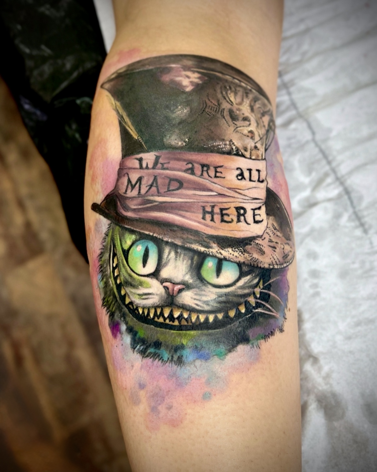 Watercolor Tattoo Deggendorf — Aquarell Cheshire Cat mit Zylinder 'We are all mad here' Wade, Tattoo Studio Deggendorf Luca Limito, Atelier Voltaire Tattoo Studio / Watercolor tattoo Deggendorf — Cheshire Cat with top hat 'We are all mad here' on calf by Luca Limito at Atelier Voltaire Tattoo Studio