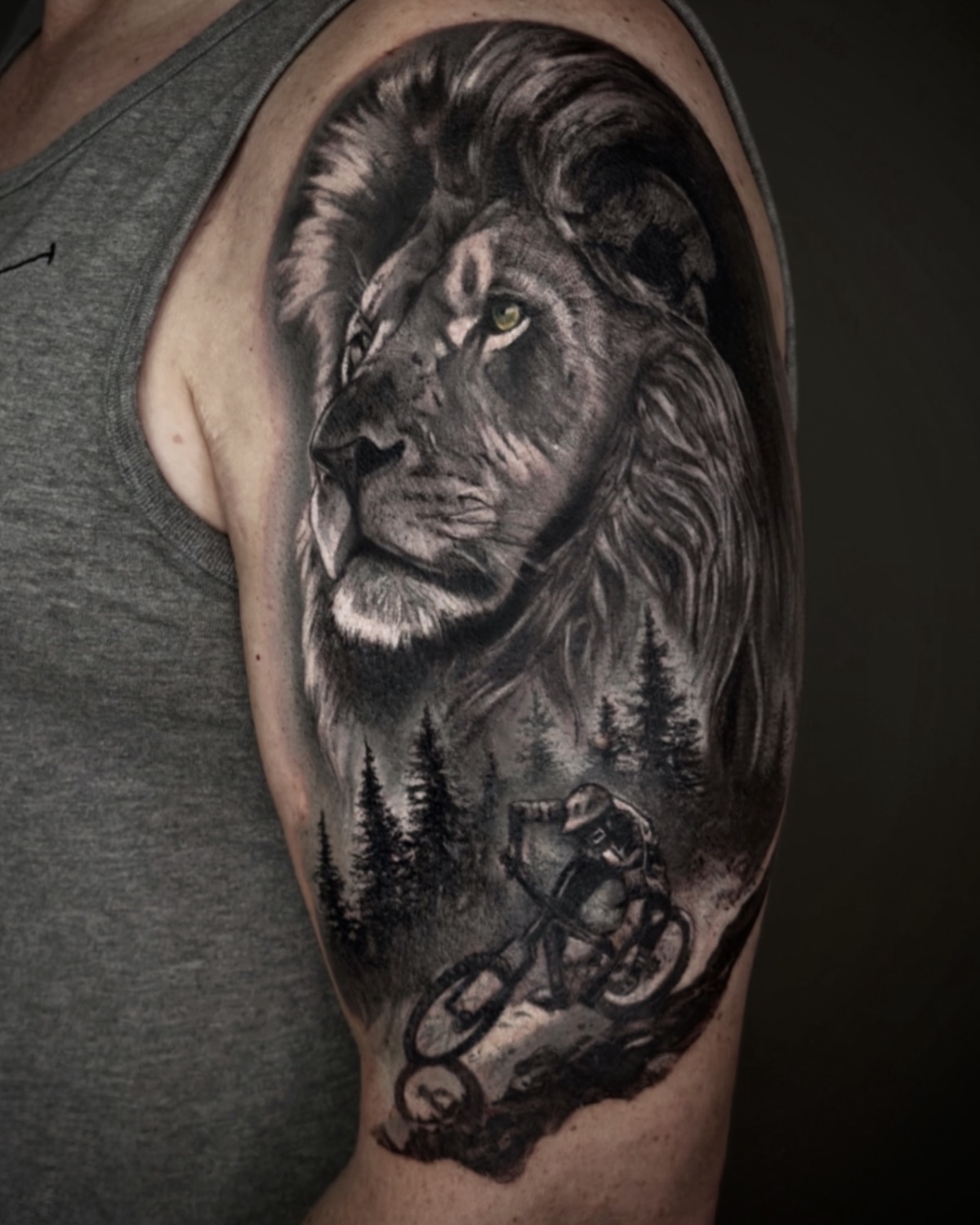 Tier Tattoo Deggendorf — hyperrealistischer Black & Grey Löwenkopf mit Wald und Mountainbike-Silhouette am Oberarm von Luca Limito Tattoo, Atelier Voltaire Tattoo Studio / Animal tattoo Deggendorf — hyperrealistic black and grey lion head with forest and mountain bike silhouette on upper arm by Luca Limito at Atelier Voltaire Tattoo Studio